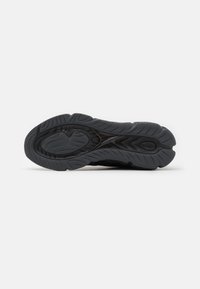 Semelle de chaussure de sport noire avec un motif texturé et rainuré pour l'adhérence, présentant un design central surélevé et des bords courbés.