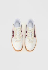 Hvite og kremfargede sneakers med perforert tå, med røde og blå detaljer på sidene og en såle av gummi.