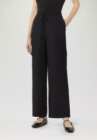 Schwarze weite Hose mit elastischem Bund und Kordelzug. Verfügt über zwei Seitentaschen und eine Cargotasche am rechten Bein.