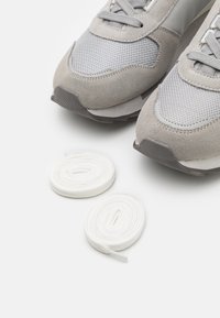 Scarpe da ginnastica grigie con tomaia in rete e suede, con lacci bianchi piatti posizionati vicini su uno sfondo semplice.