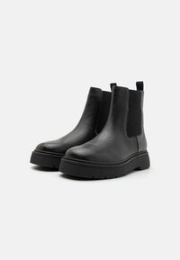 Bottines en cuir noir avec des panneaux élastiques sur les côtés, un bout rond et une semelle en caoutchouc épaisse, présentant une finition texturée et une languette.