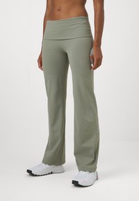Persona vistiendo pantalones anchos color verde salvia con una cinturilla alta y zapatillas deportivas blancas sobre un fondo plano.