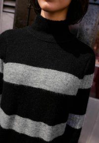 Schwarz-grauer gestreifter Pullover aus weichem, strukturiertem Stoff. Verfügt über einen hohen Kragen und sichtbare Rippungen an den Bündchen und dem Saum.