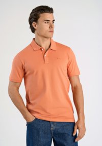 Polo a maniche corte in corallo, realizzato in cotone liscio. Presenta un colletto classico, tre bottoni e un piccolo logo sul petto.