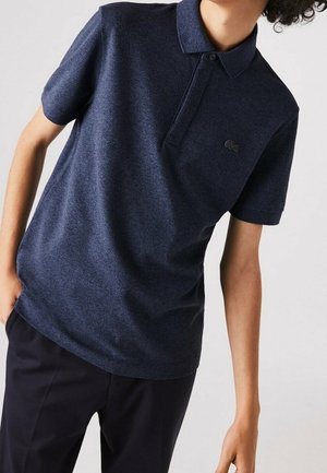 Granatowa koszulka polo z teksturowanej tkaniny, z krótkimi rękawami, kołnierzykiem oraz małym haftowanym logo na piersiach; w połączeniu z ciemnymi spodniami.
