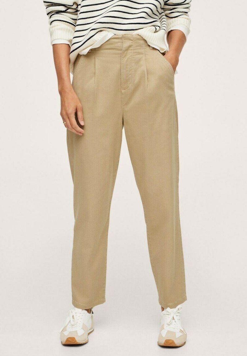 Beige, hochgeschnittene Hose mit geradem Bein, versehen mit Vorderfalten und Seitentaschen, kombiniert mit weißen Sneakers.
