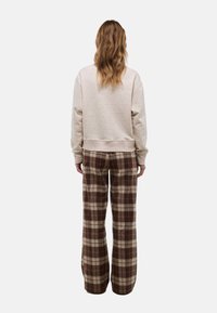 Sweatshirt beige clair en tissu texturé, associé à un pantalon à carreaux marron taille haute avec des jambes larges et une coupe décontractée.