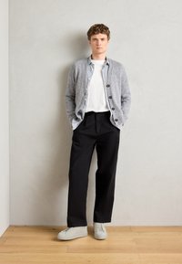 Pull gris sur une chemise rayée, t-shirt blanc, pantalon noir et baskets gris clair. Textures douces et coupe décontractée.