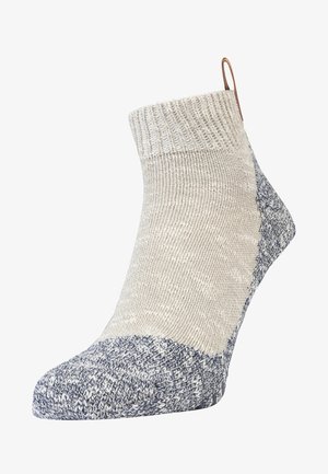 Beige kniehohe Socke mit strukturiertem Obermaterial und einem dunkelblauen melierten Bund und Zehen. Verfügt über eine kleine Schlaufe an der Rückseite für ein einfaches Anziehen.