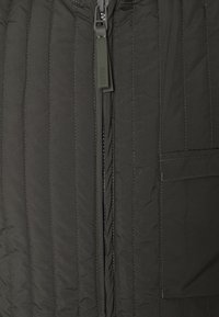 Czarna pikowana kurtka z pionowymi przeszyciami, z zamek błyskawicznym z przodu i boczną kieszenią. Wykonana z lekkiego, wodoodpornego materiału.