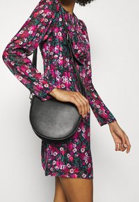 Mekko on koristeltu eloisalla kukkakuviolla, jossa on vaaleanpunaisia, valkoisia ja vihreitä sävyjä mustalla taustalla; yhdistetty pyöreään mustaan olkalaukkuun.