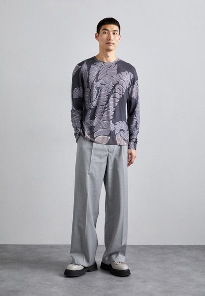 Tricou cu mânecă lungă și model gri de frunze; pantaloni gri; încălțăminte masivă cu o talpă texturată; fundal neutru.