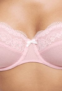 Roze kant BH met een mesh ontwerp, bloemmotieven, gegolfde randen en een klein strikje in het midden. De stof lijkt zacht en textuur te hebben.