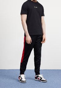 Musta lyhythihainen t-paita, jossa on "AIR"-logo, yhdistettynä mustiin collegehousuihin, joissa on punaiset sivuraidat, sekä valko-mustiin tennareihin, joissa on punaisia yksityiskohtia.