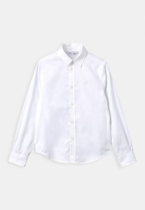 Camisa blanca de manga larga hecha de algodón con cuello abotonado, que presenta un dobladillo curvado y un discreto logo en relieve en el pecho.