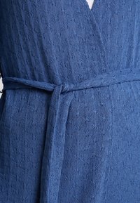 Vestido envolvente azul con textura, que incluye un cinturón para atar, con un patrón sutil y un diseño de escote en V, fabricado con una tela suave y ligera.