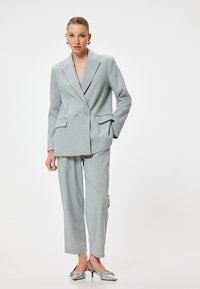 Blazer double boutonnage gris clair avec revers crantés, assorti à un pantalon large. Texture lisse, coupe ajustée et motif subtil.