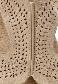 Bota de ante beige con patrones recortados, cierre de cremallera suave en la parte trasera y superficie interior texturizada.