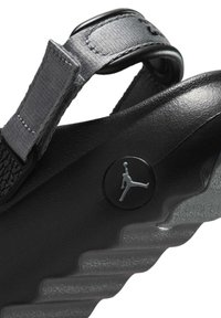 Svart sandal med texturerad rem och glänsande finish. Har en rund logotyp med en silhuett och en vågig sula för ökat grepp.