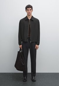 Black bomber jacket with a zip, brown knit shirt, navy trousers, and a dark suede tote bag. Smooth texture and minimalistic design.