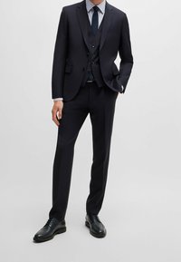 Trojdílný námořnicky modrý oblek s na míru střiženým sakem, tříknoflíkovou vestou a úzkými kalhotami. Kombinován s světle modrou pruhovanou košilí a černými botami.