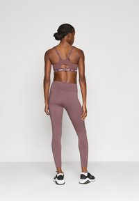 Bronzen sportbeha met verstelbare bandjes en uitsnijdingsdetail, gecombineerd met bijpassende high-waisted leggings van zachte, rekbare stof. Zwarte sneakers.