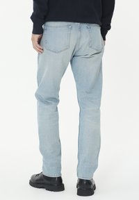 Šviesiai mėlynos džinsinės kelnės su tiesiu praktišku pjūviu, turinčios galines kišenes ir lengvą išblukimą. Dėvimos su juodomis raištelių botais.