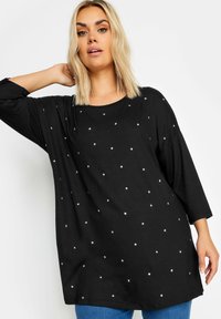 Musta pitkähihaiseksi paita pehmeästä kankaasta, jossa on hajallaan valkoisia tähtiä, pyöreä kaula-aukko ja rento, löysä malli.