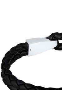 Svart flätat läderarmband med ett stilrent silverlås med stämplat märke. Designen kombinerar textur och kontrasterande material.