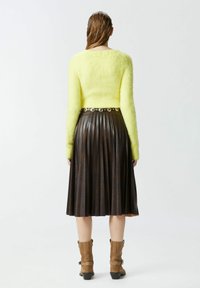 Svijetložuta krznena veste, nabranu smeđu kožnu suknju, smeđe suknje od antilopa s kopčama, glatke teksture i kontrastni materijali.