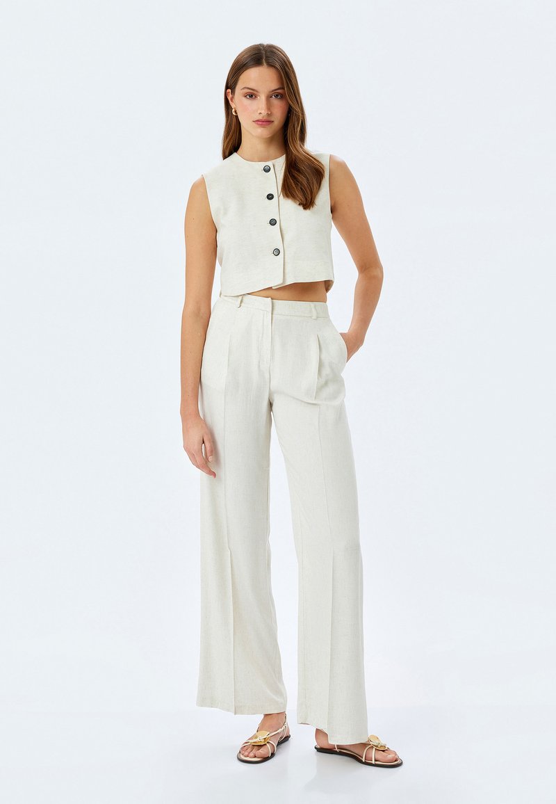 Lichtgekleurde cropped vest met knoopsluiting, gecombineerd met hooggezette, wijde broek. Glad stof met een subtiele textuur.