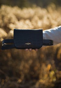 Czarna torebka z imitacji skóry z teksturowanym wzorem krokodyla, z klapą i złotym logo. Torebka ma regulowany pasek.