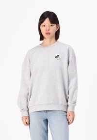 Szürke pulóver, puha anyagból készült, kerek nyakkivágással és hosszú ujjakkal. A mellrészén egy kis fekete-fehér Mickey Mouse logó található.