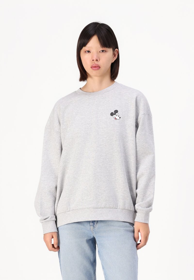 Szürke pulóver, puha anyagból készült, kerek nyakkivágással és hosszú ujjakkal. A mellrészén egy kis fekete-fehér Mickey Mouse logó található.