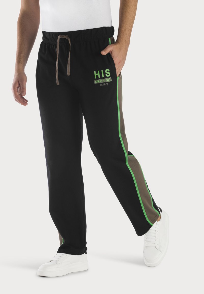 Schwarze Jogginghosen mit grünen und braunen Seitenstreifen, elastischem Bund mit Kordelzug und "H.I.S ATHLETIC DEPT. CHAMPS" in Grün gedruckt.
