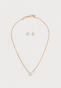 Gold chain necklace with a round pendant featuring a clear stone; matching gold stud earrings with a similar stone detail.