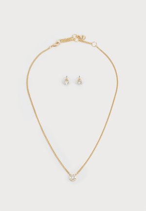Collana in oro con un pendente rotondo dotato di una pietra trasparente; orecchini a chiodo in oro abbinati con un dettaglio simile della pietra.