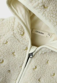 Krämfärgad, fluffig fleece-babyhoodie med foder i huvan, dragkedjeslutning och små gula halvmånemönster. Etiketten säger "Lil’Atelier."