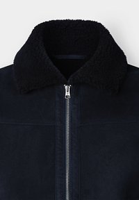 Donker marineblauwe jas met een zachte zwarte kraag, met een volledige ritssluiting en een gladde suèdetextuur. Geen zichtbare patronen of accenten.