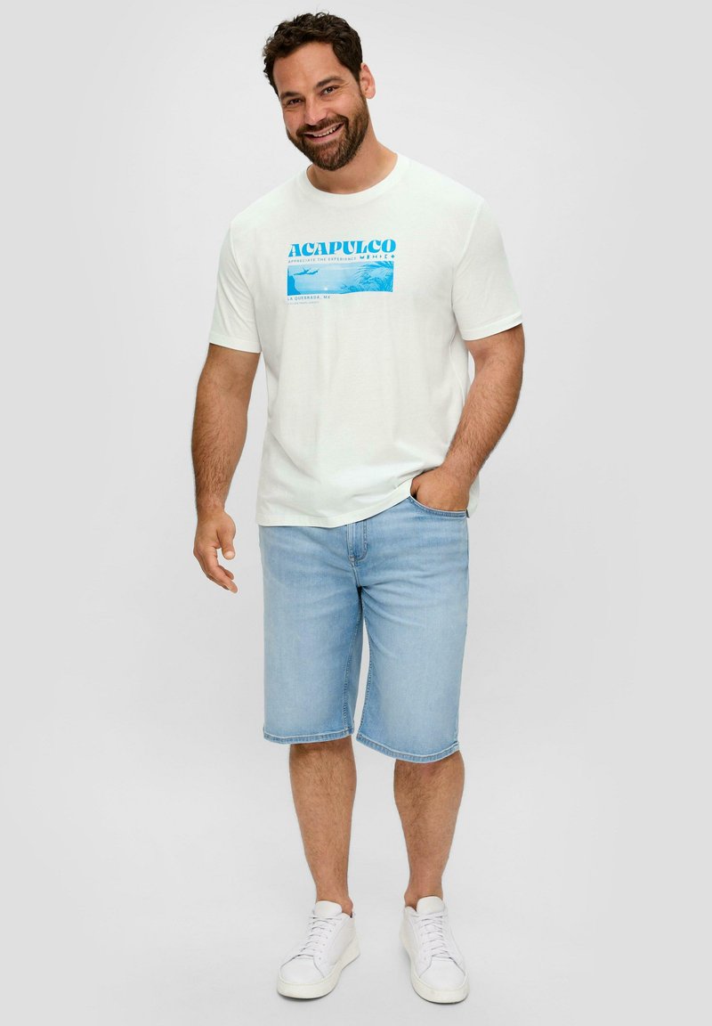Weißes T-Shirt mit kurzen Ärmeln und blauem "Acapulco"-Grafik, kombiniert mit hellblauen Denim-Shorts und weißen Sneakers, vor einem neutralen Hintergrund stehend.
