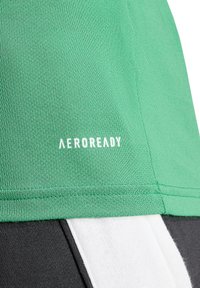 Top sportivo verde AEROREADY con tessuto testurizzato, logo stampato in bianco e inserti a pannello in bianco e nero.