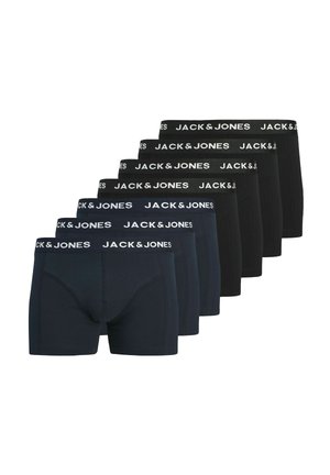 Skjorteløs mand med kort krøllet hår iført marineblå Jack & Jones boxer, stående mod en ensfarvet grå baggrund.