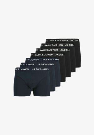 Homme torse nu aux cheveux courts et bouclés portant des boxers bleu marine Jack & Jones, debout devant un fond gris uni.