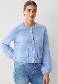 Lichtblauwe, gebreide cardigan met een ronde halslijn, knoopsluiting, twee voorzakken en geribbelde zomen. Zachte textuur met een ontspannen pasvorm.