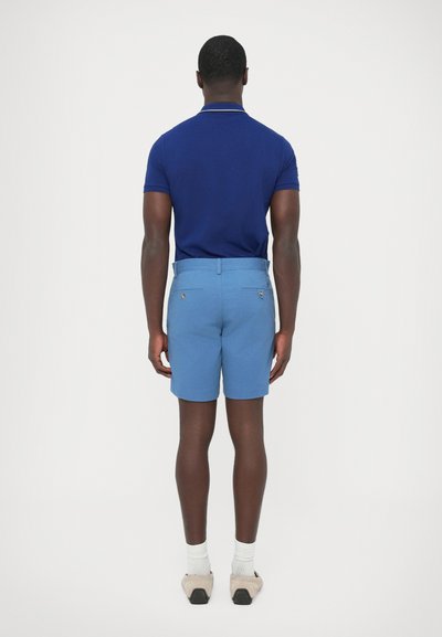 Modré šortky s hladkým predným dielom a dvoma zadnými vreckami, doplnené priliehavým modrým polokošeľou s kontrastným golierom.