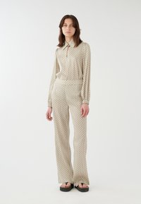 Blouse à motifs beige clair avec col et détail en trou de serrure, assortie à un pantalon large. Les deux présentent un imprimé géométrique.