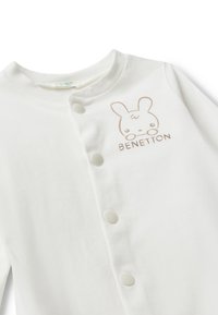 Body de algodón blanco para bebé con cuello redondo, botones de presión en la parte frontal y un gráfico de un conejo marrón claro con el texto "BENETTON".
