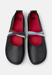 Svarta läderballerina har korsade elastiska band i blått och brunt, med en livlig röd innersula. Rund tå och minimalistisk design.