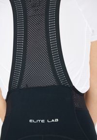 Schwarze sportliche Bib-Shorts aus dehnbarem Material mit Netz-Akzenten. Verfügt über ein Logo, flache Nähte und breite Träger für Unterstützung.