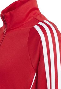 Rode sportieve jas met een hoge kraag, ritssluiting aan de voorkant en een witte driekleurige ontwerp op de schouders. Gemaakt van textuurstof.